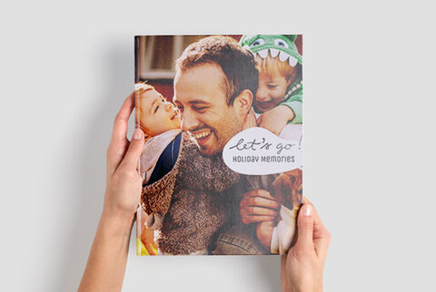 Ein Mensch hält ein CEWE FOTOBUCH mit der Aufschrift 'let's go! HOLIDAY MEMORIES'