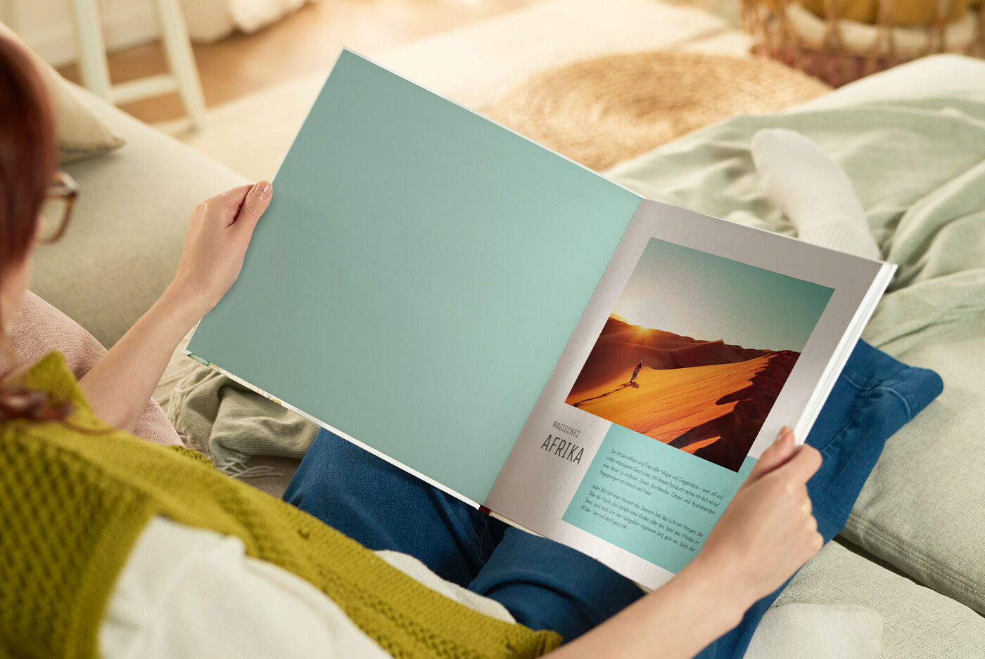 Person blättert auf dem Sofa im CEWE FOTOBUCH, Seite mit Wüstenfoto und Überschrift Afrika