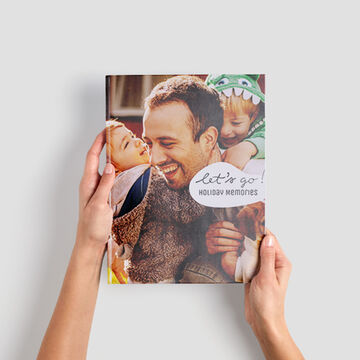 Ein Mensch hält ein CEWE FOTOBUCH mit Urlaubsbildern.