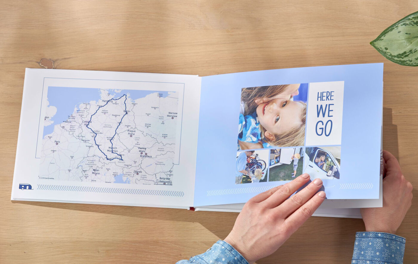 Eine Person blättert durch ein CEWE Fotobuch mit Reisemomenten und einer Karte.