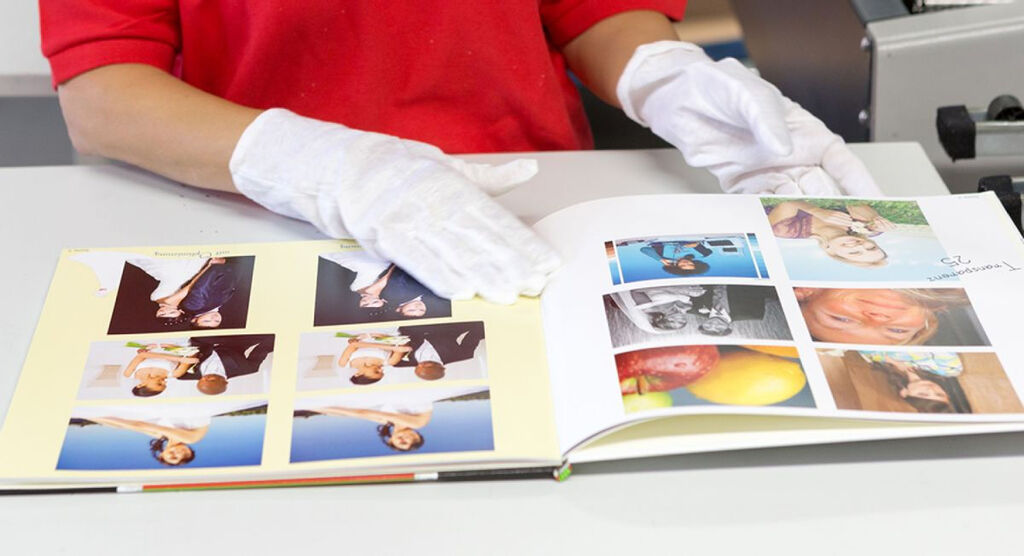Eine Person blättert durch ein CEWE FOTOBUCH, das schöne Erinnerungen zeigt, während sie Handschuhe trägt