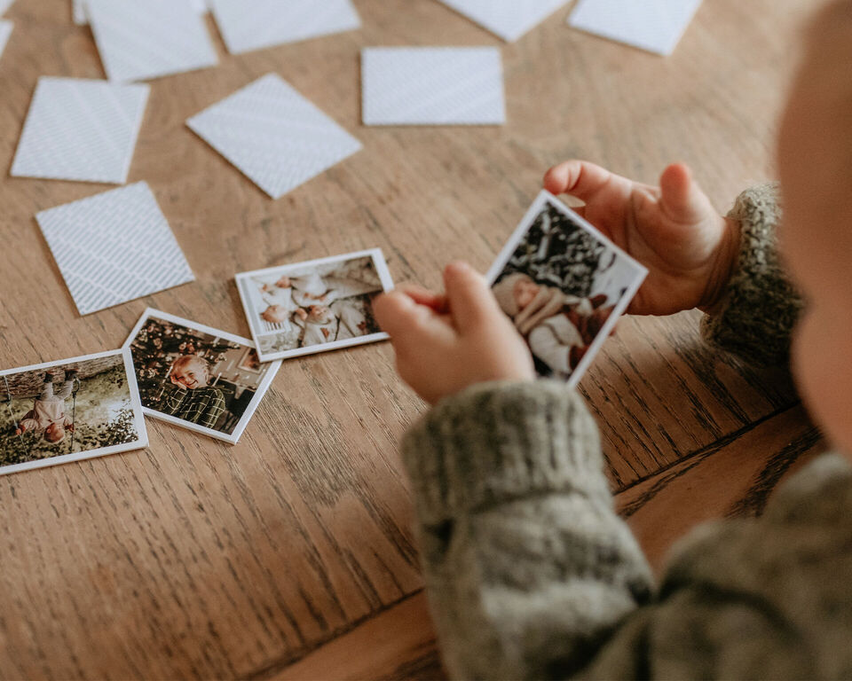 Ein Kind spielt mit Fotokarten auf einem Holztisch und betrachtet die Bilder.