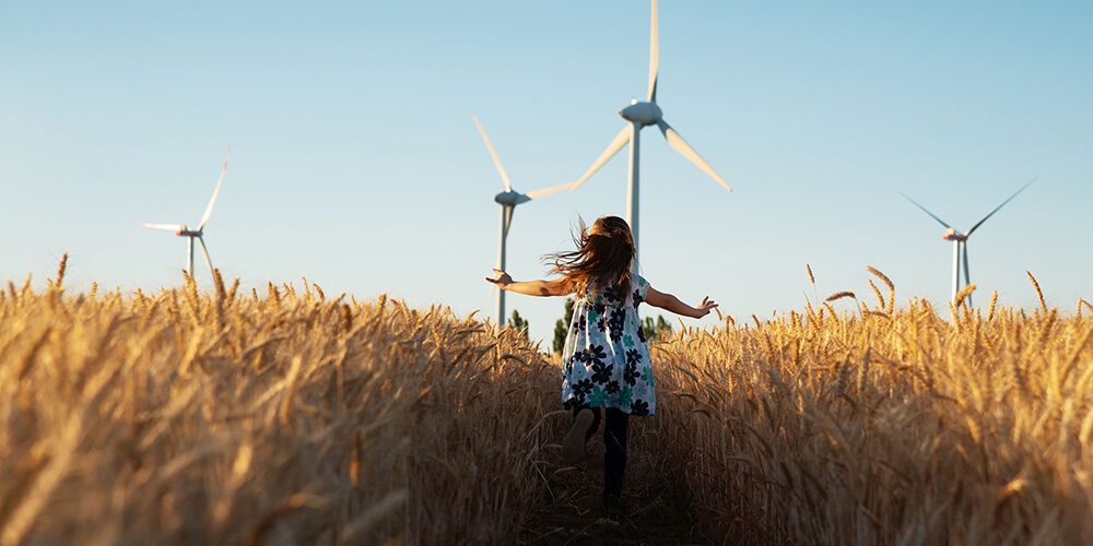 Ein Mädchen in einem blühenden Feld mit Windrädern im Hintergrund, sie betrachtet fröhlich die Natur.