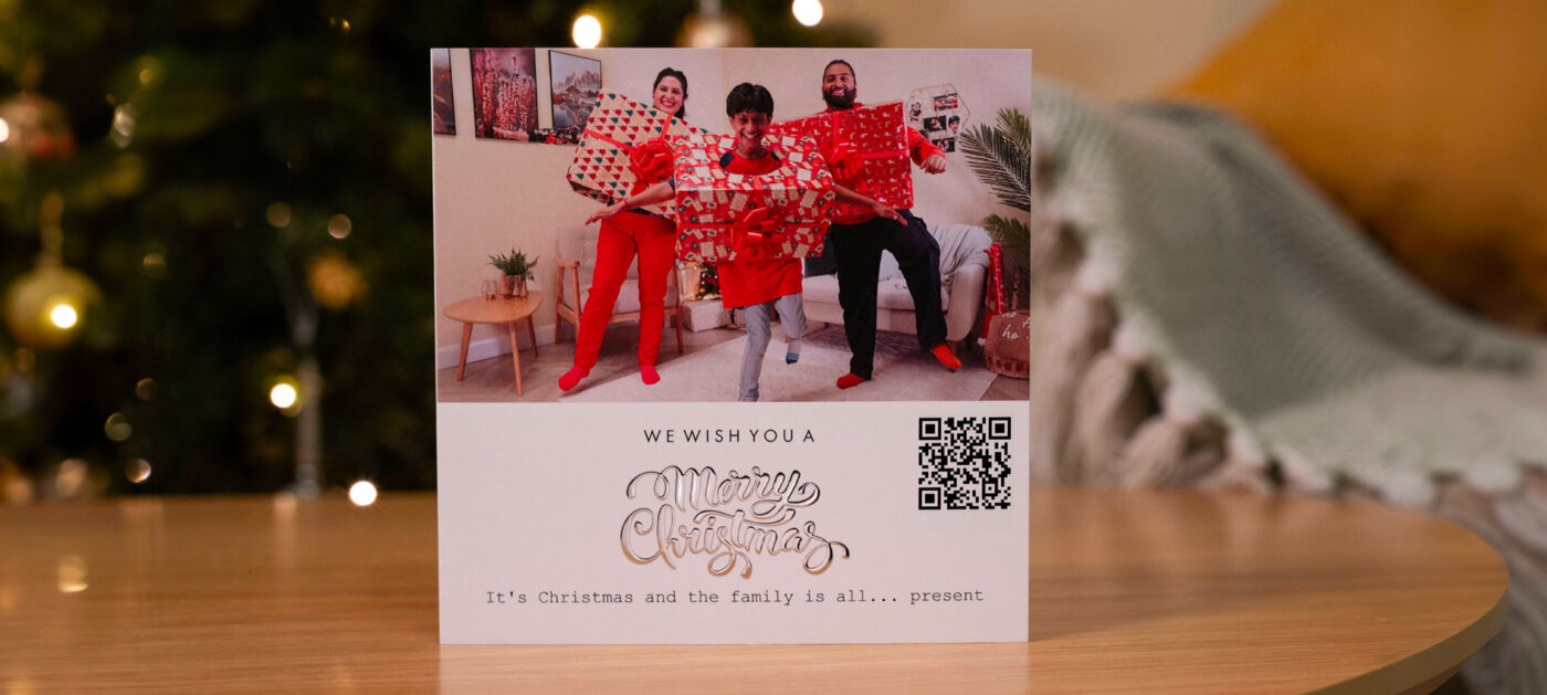 Drei fröhliche Personen in roten Outfits mit Geschenken und einer Weihnachtsbotschaft
