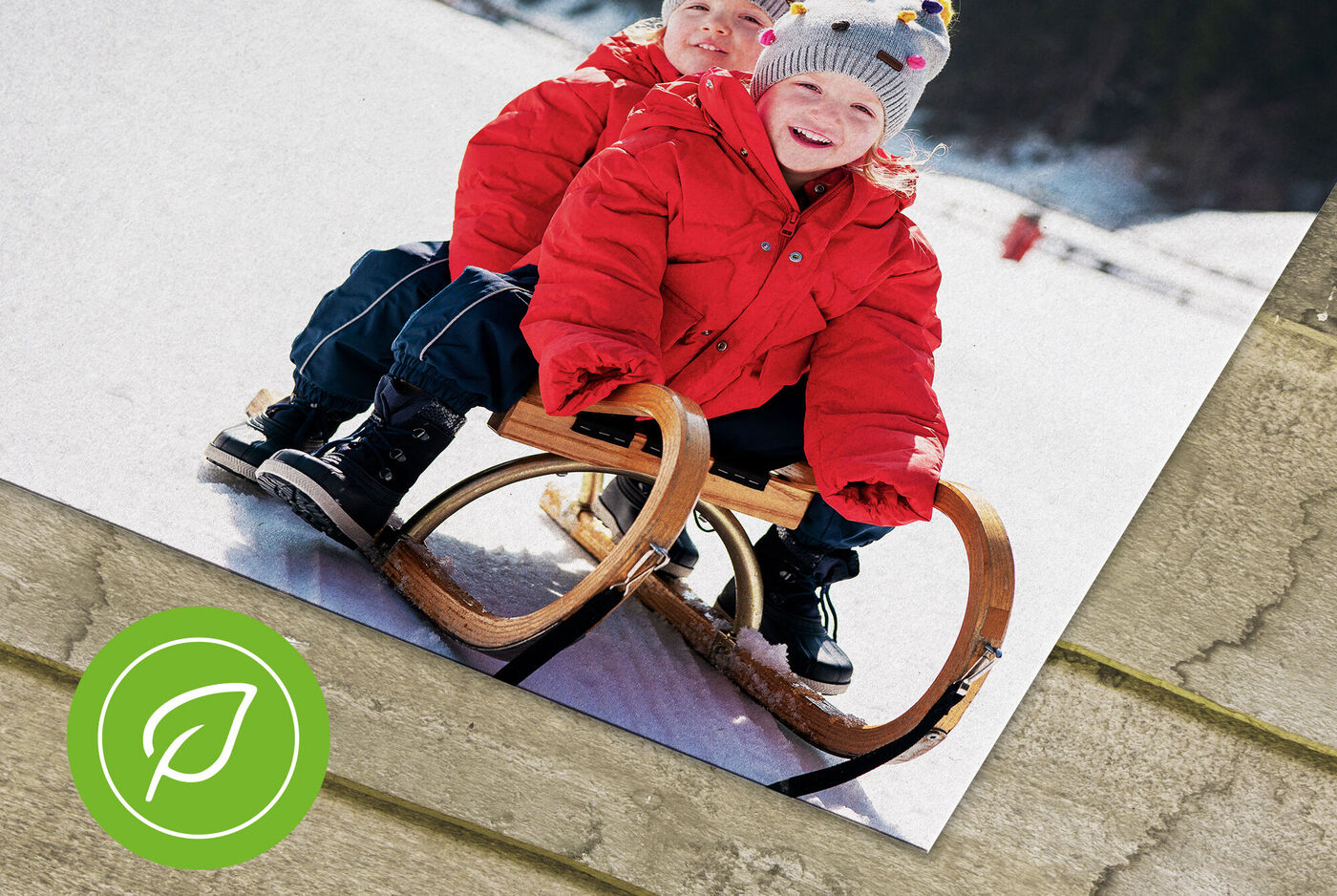 Zwei Kinder in roten Jacken auf einem Schlitten im Schnee.