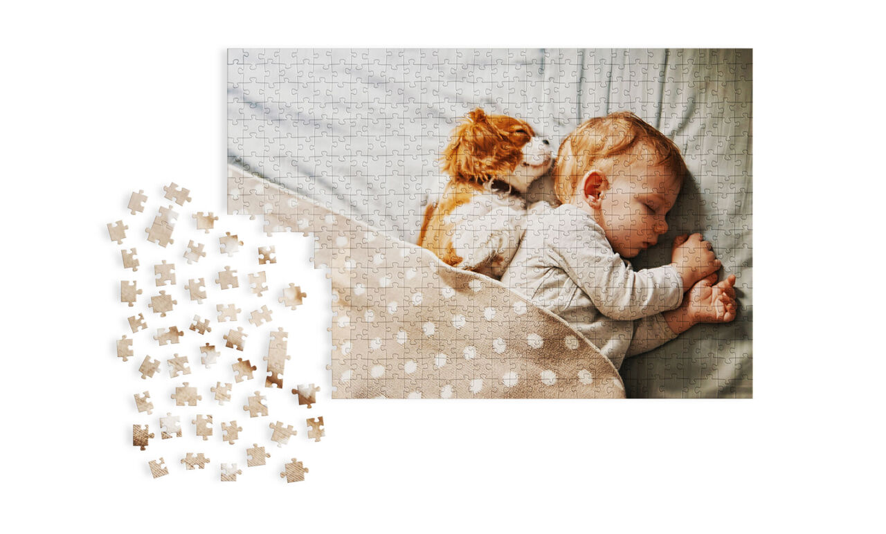 Ein schlafendes Baby liegt auf einem Bett, umgeben von einem weichen, gepunkteten Bettbezug. Ein kleiner Hund kuschelt sich an das Baby.