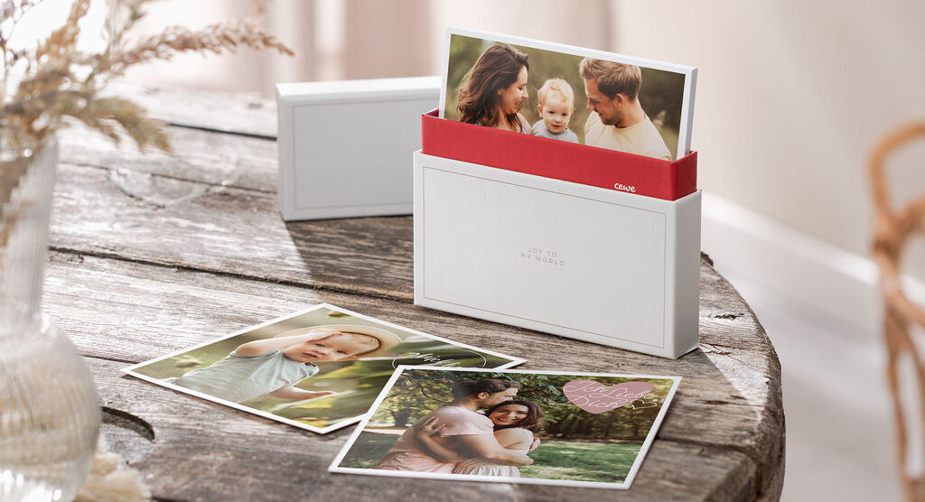 CEWE Grußkarten in einer weißen Box auf einem Holztisch, umgeben von weiteren Fotokarten