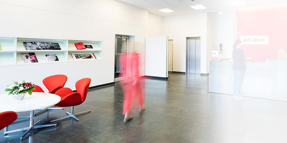 Bright reception area with red chairs, a plant on a table, and a reception desk.